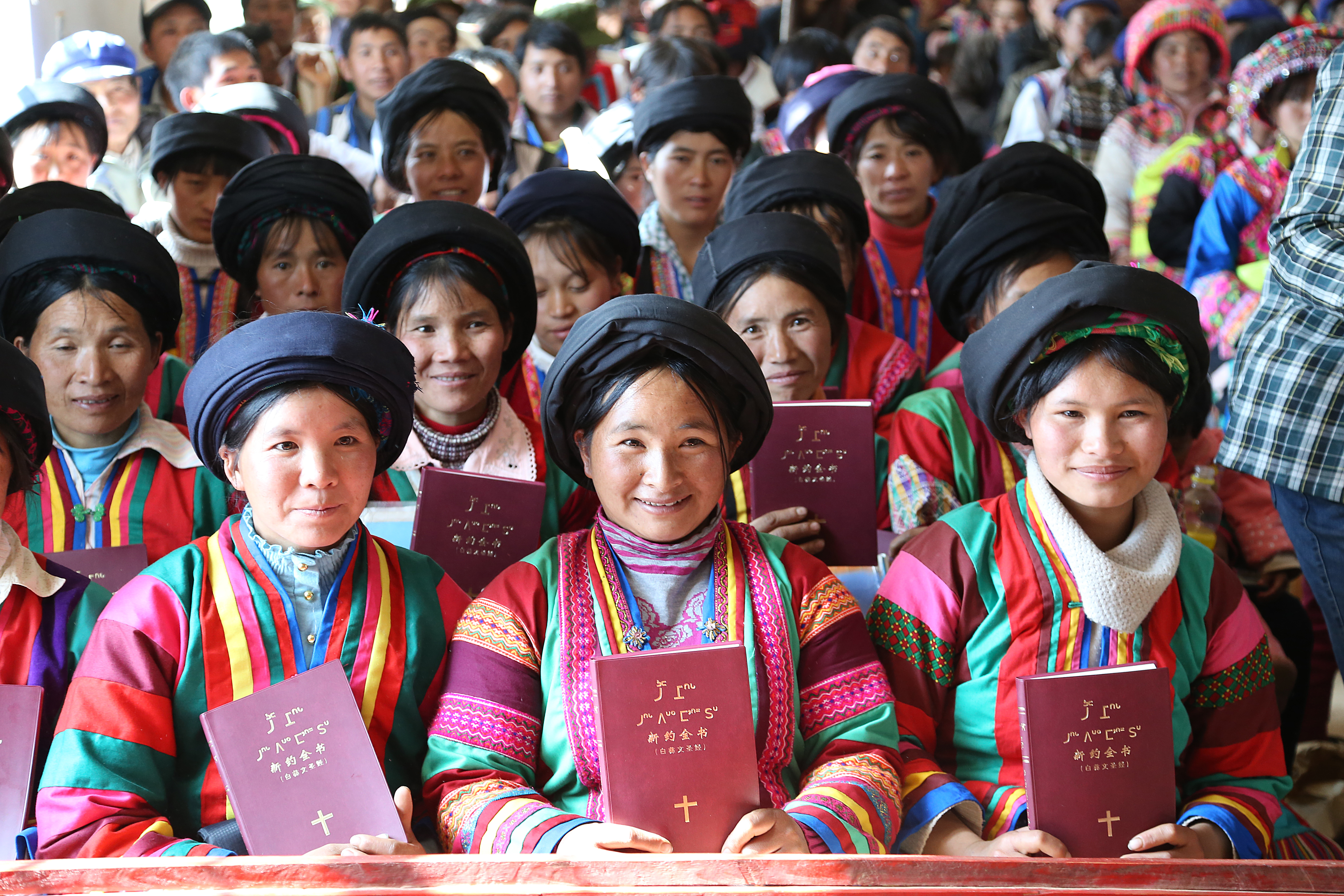 Iloisia ihmisiä kirkon penkissä. He ovat juuri saaneet omat valkoisen lin kieliset Raamatut.