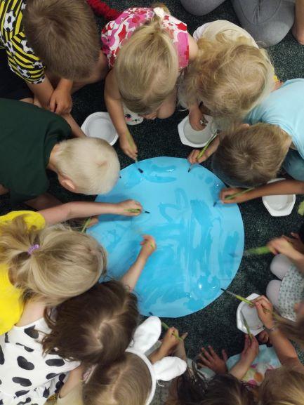 Lapset maalaavat vedellä pyöreäle kartongille yhteistä maalausta.