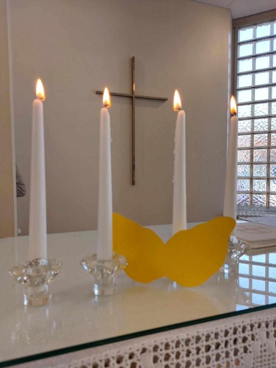 Veikkolan seurakuntakodin alttarilla palaa neljä kynttilää. Kynttilöiden välissä on pienet enkelinsiivet.