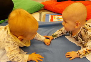 Kaksi vauvaa vatsallaan lattialla katsoo toisiaan silmiin ja melkein koskettaa käsillään. 