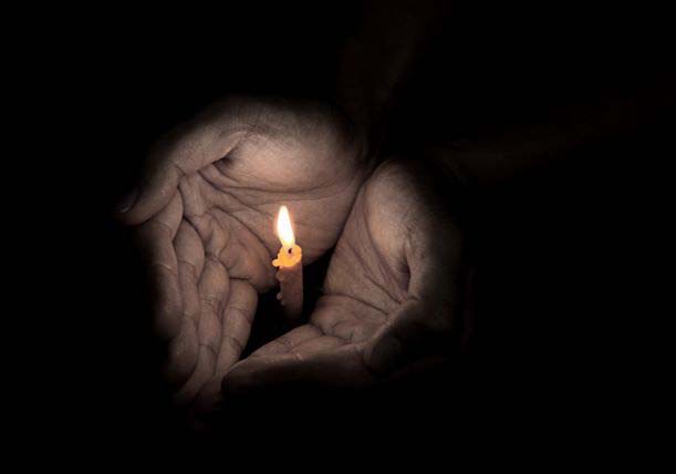 Ihmisen kädet suojaavat palavaa kynttilää.