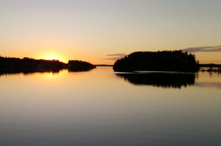 Auringonlasku heijastuu peilityynen järven pintaan