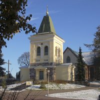 Kirkkonummen kirkko Talvisessa maisemassa keltainen kellotapuli, joka takaa näkyy kivikirkon pääty.