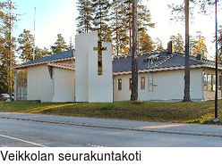 Veikkolan seurakuntakoti Korkeiden mäntyjen ympäröimä matala vaaleaseinäinen rakennus.