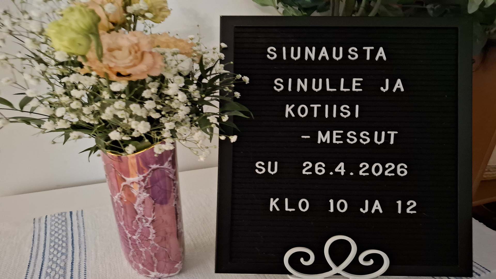 Kukkia ja kyltti, jossa lukee Siunausta sinulle ja kotiisi -messut su 26.4.2026.
